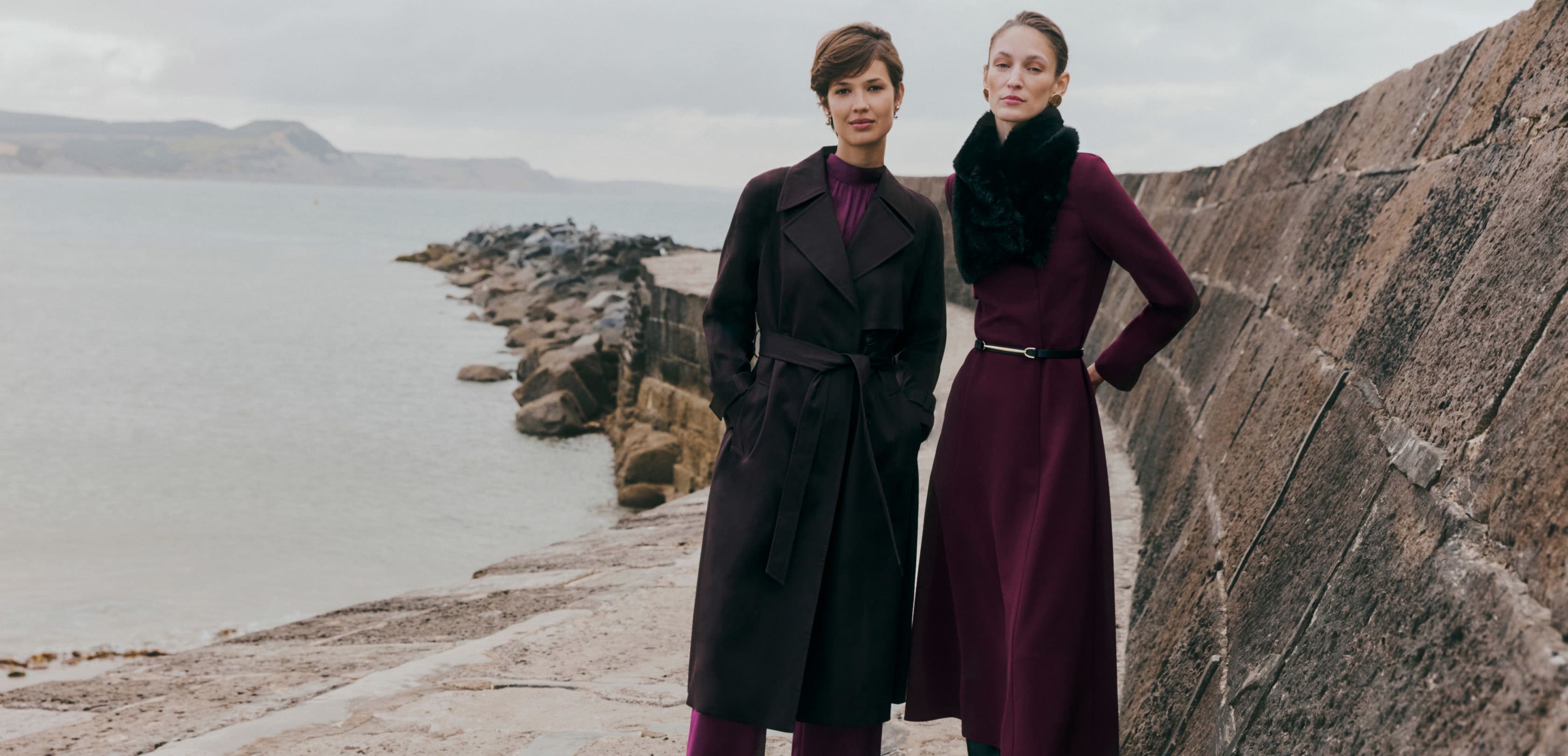 Image of two models standing on the British coast wearing long wool coats.