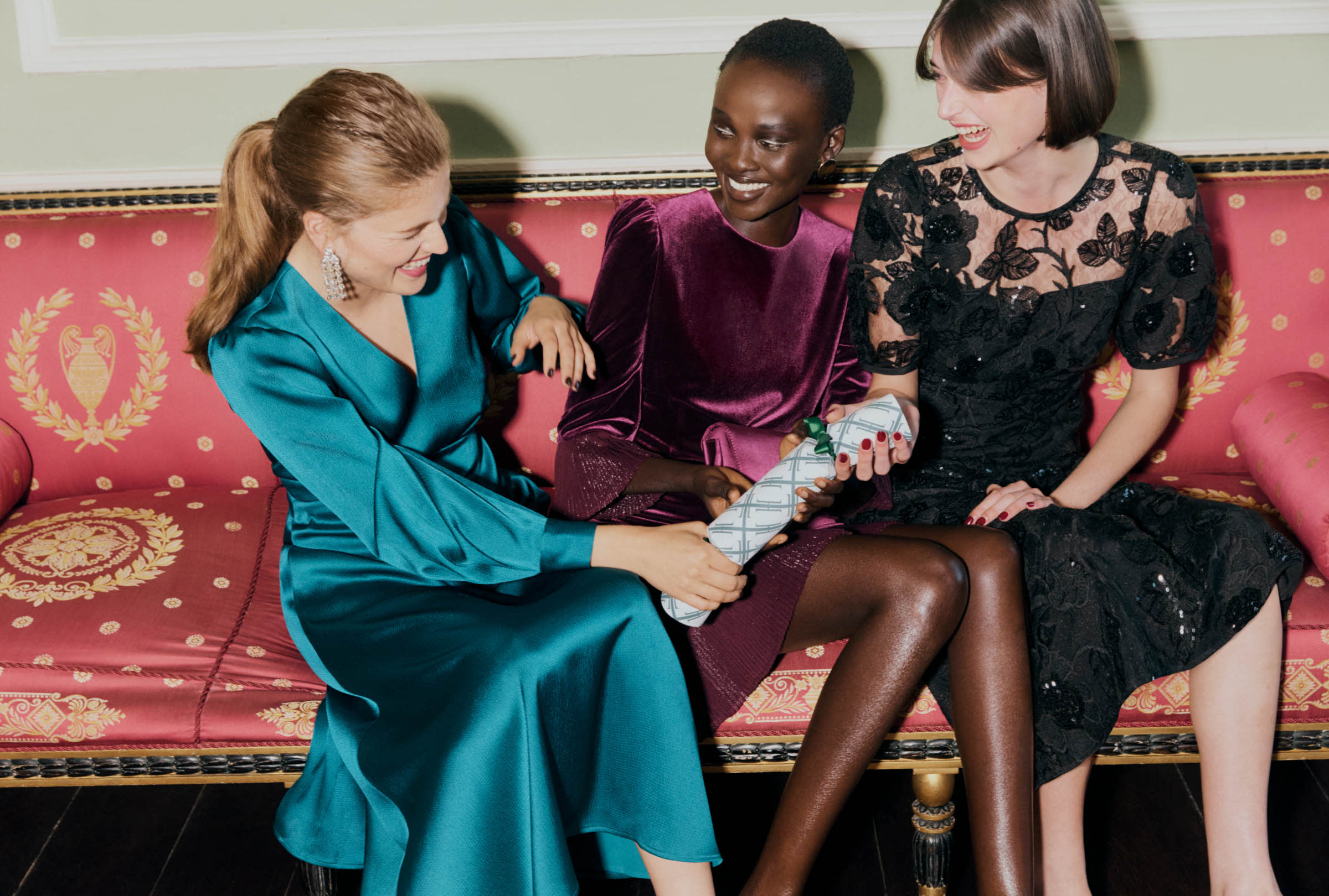 An image of three models in party dresses sitting down to pull a cracker.