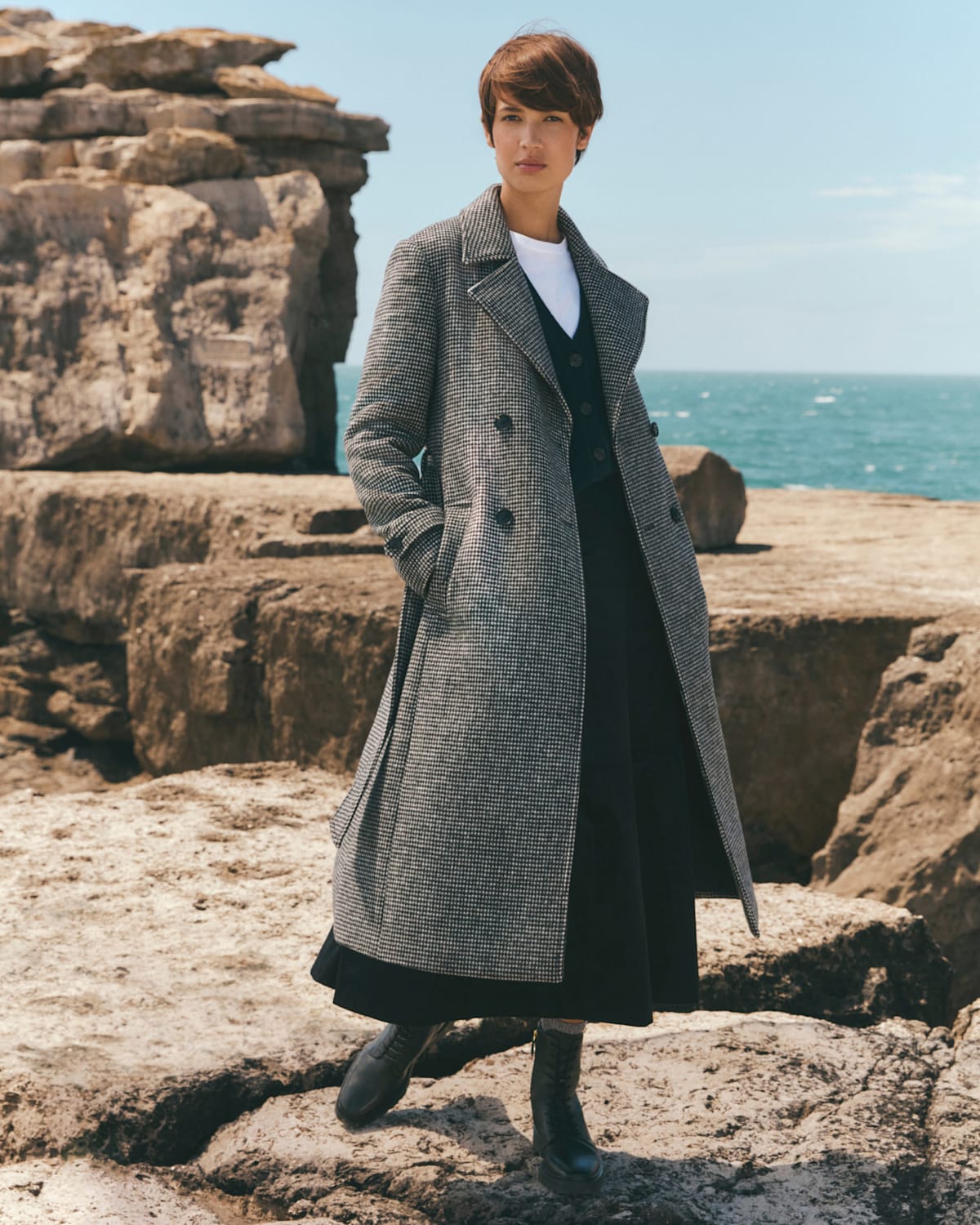 Image of model walking on a rugged coastal path wearing a dogtooth wool coat.