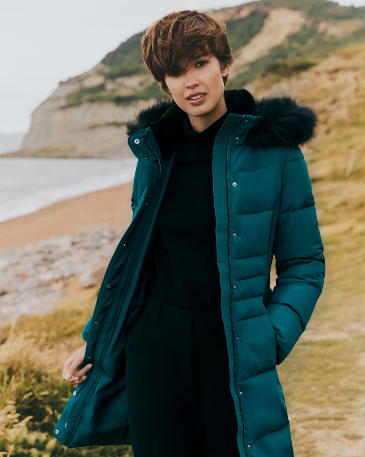 Image of a model standing outside on the coast in a puffer jacket.