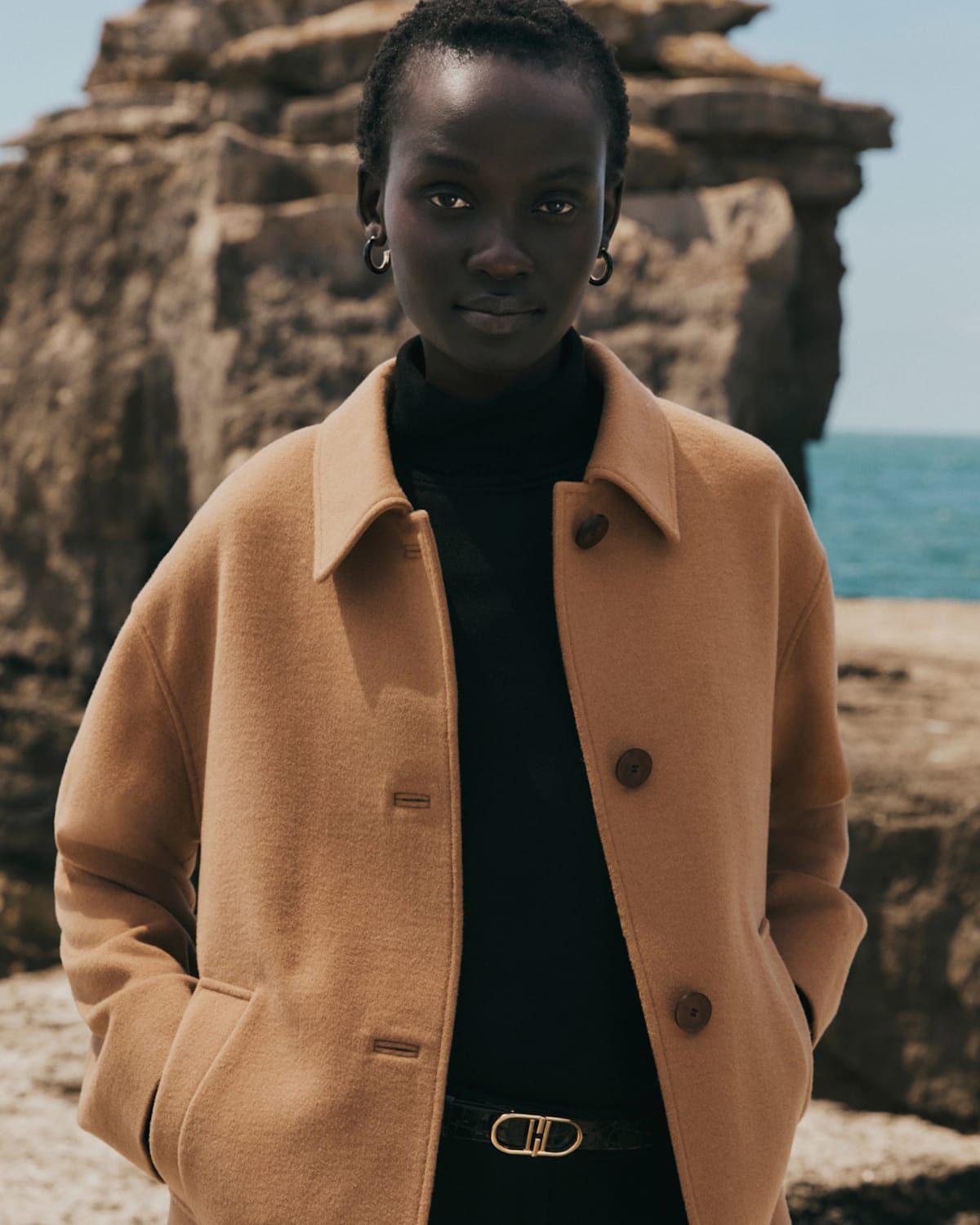 A model wearing a long coat with a faux fur collar over tailoring.