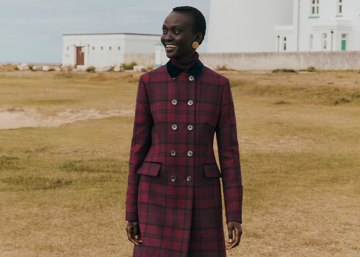 Image of a model on the coast wearing a long, wool, check coat.