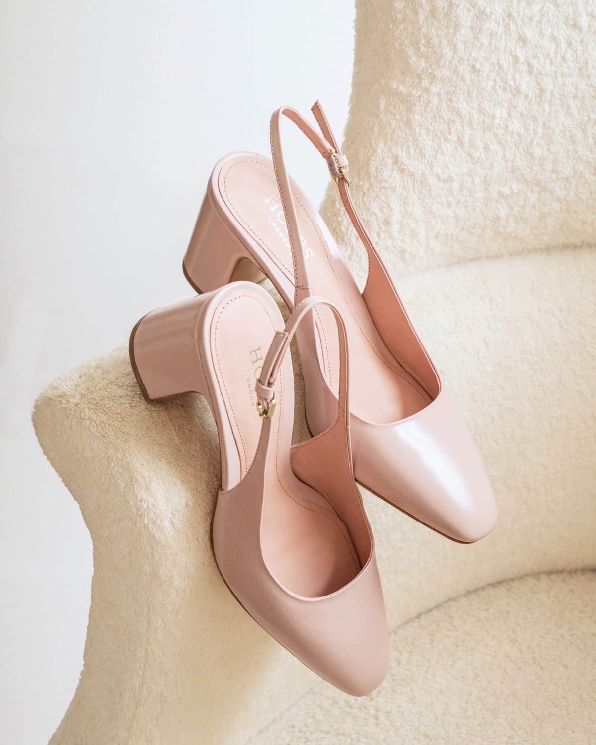 A pair of blush pink patent slingback shoes photographed on the arm of a chair.